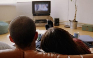 Young couple watching television at home, rear view (focus on heads).